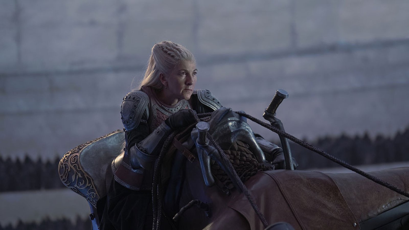 A woman with white hair rides on the back of a dragon indoors.