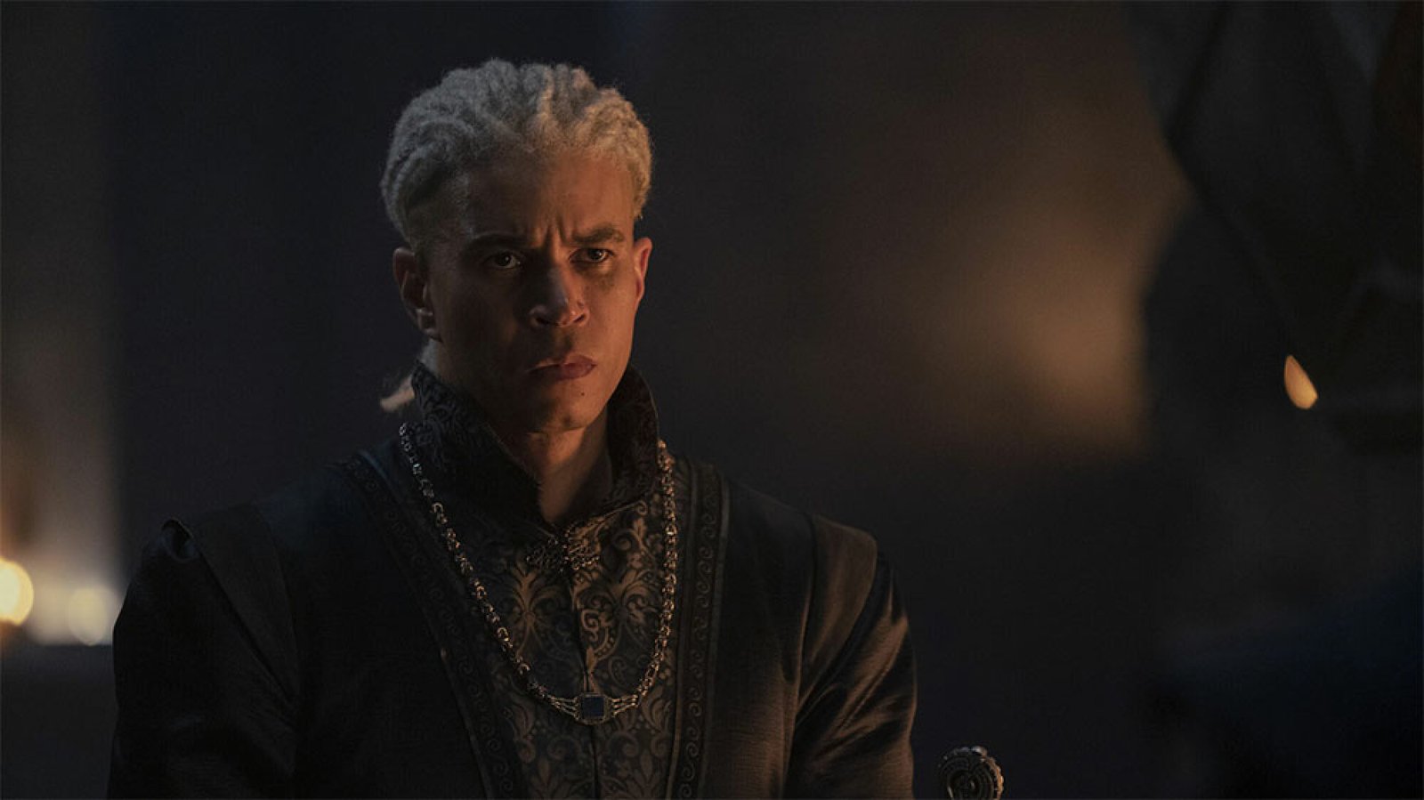 A man with white hair stands in a dark room.